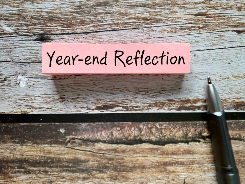 Sticky note with the words “Year-end Reflection” placed on a wooden desk, symbolising a review of achievements, lessons learned and progress over the first year of the IFIGENEIA project.